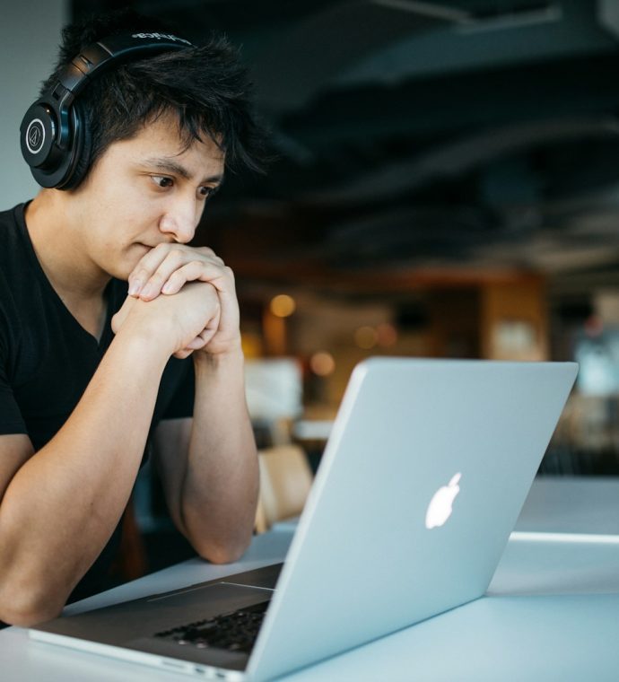 man wearing headphones while sitting on chair in front of MacBook